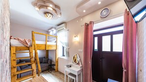 A room with bunk beds, a desk, a chair, a small table, a mirror, and a door with curtains.