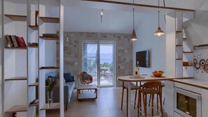 Een moderne keuken met witte kasten, een eethoek met een ronde tafel en stoelen, en uitzicht op de omgeving door een glazen deur.