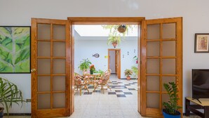 Una porta de fusta oberta que dona a una zona de menjador amb terra de pissos, cadires de vimet i plantes en testos.