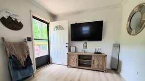 A room with a wooden floor, a TV mounted on the wall, a door with a white frame, and a small cabinet with drawers. - Private/Between PF & Knox/DOG friendly/creek/large yard (Seymour)