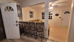 A kitchen with a bar area, wooden flooring, and a door with a welcome sign. - Private/Between PF & Knox/DOG friendly/creek/large yard (Seymour)