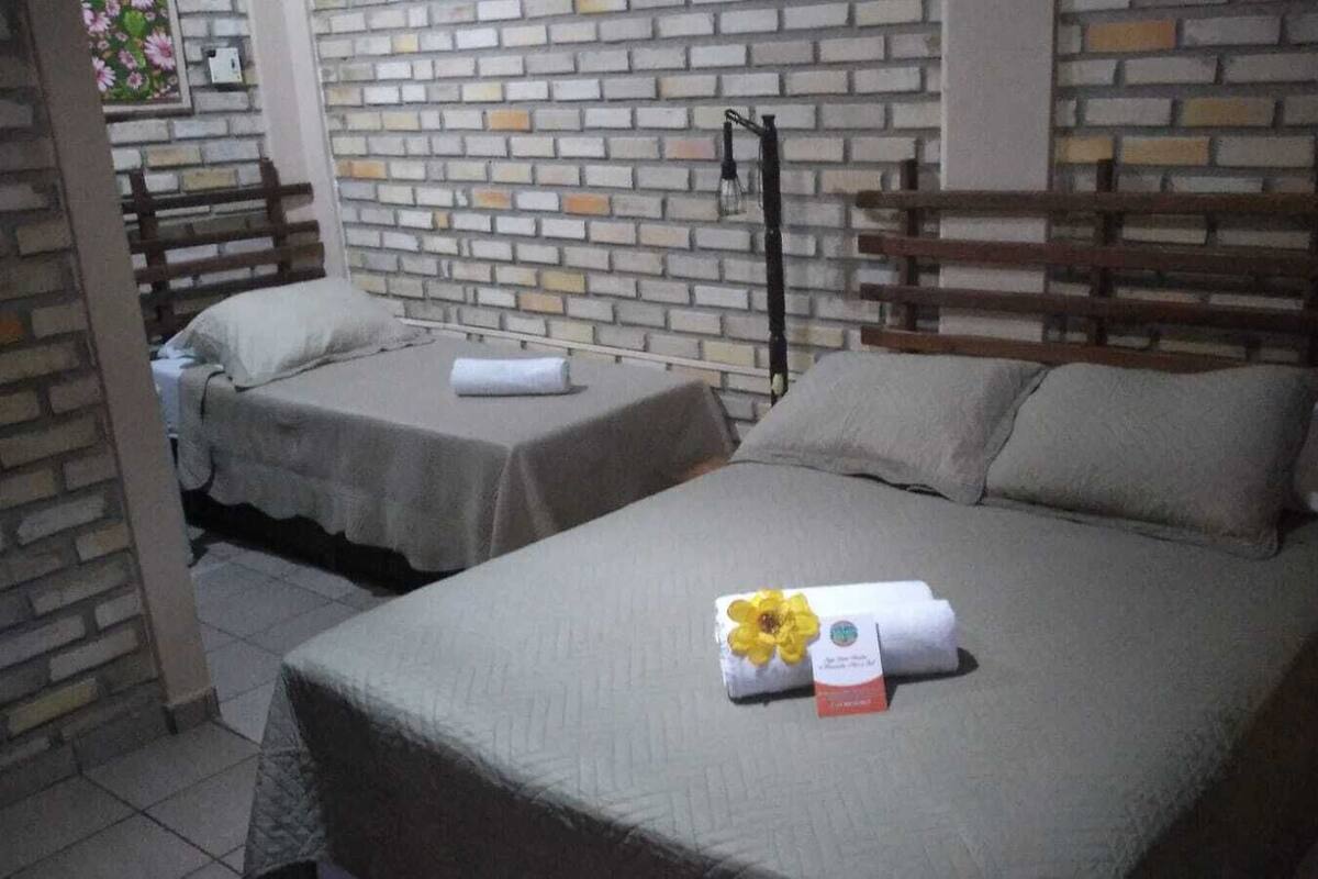 A hotel room with two beds, each with a pillow and a rolled towel. There is a brick wall behind the beds and a wooden bench in the corner.