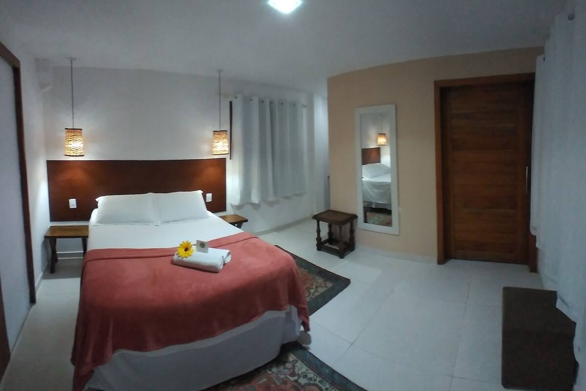 A hotel room with a large bed, bedside tables, a mirror, and a door.
