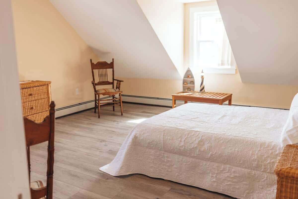 Une chambre avec un plafond en pente, un lit, une chaise, une petite table et une fenêtre.