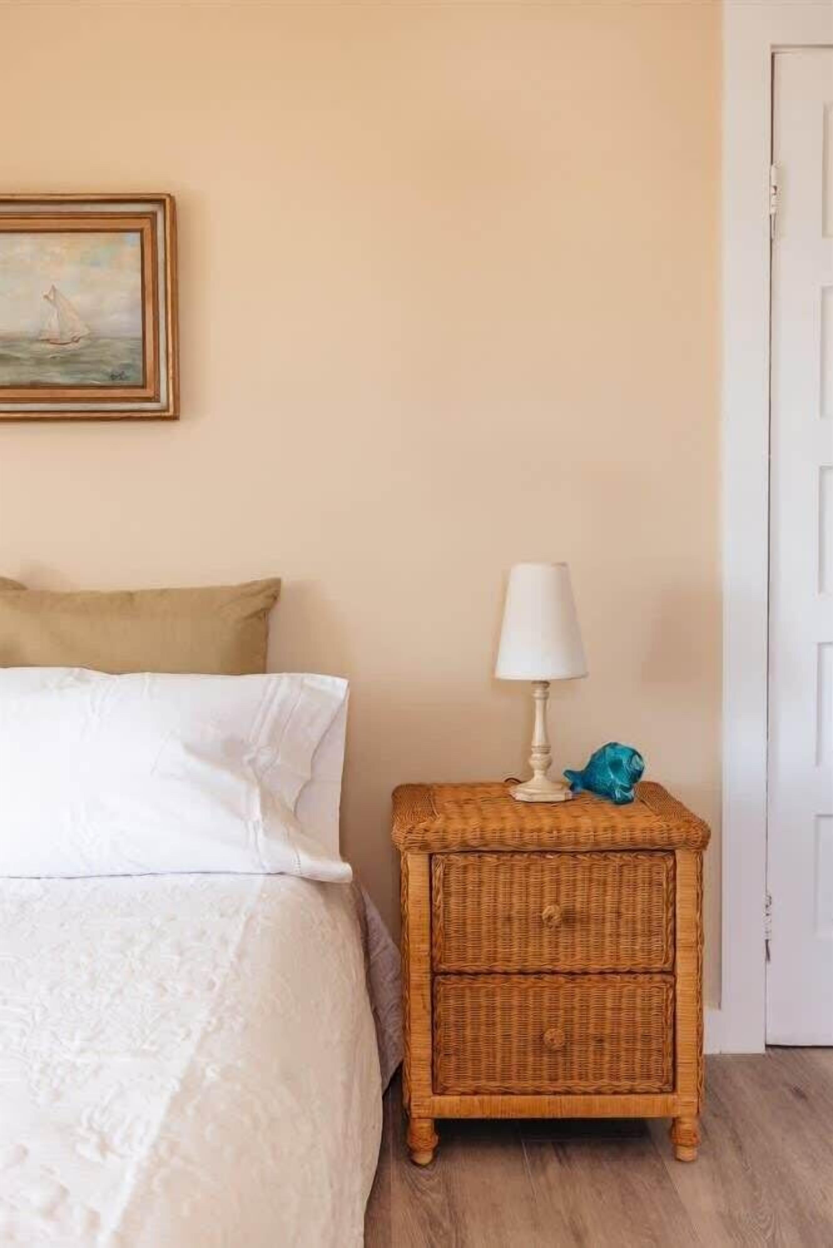 Une chambre à coucher avec un lit, une table de chevet avec une lampe, un tableau au mur et une porte.