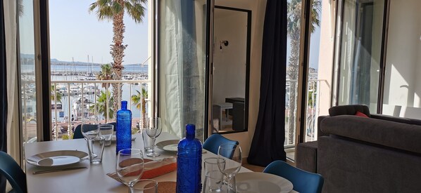 A dining area with a table set for two, overlooking a marina with boats and palm trees.