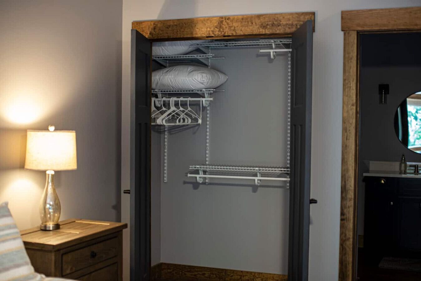 Een kamer met inloopkast, voorzien van planken, een kledingroede en een bed met lamp.