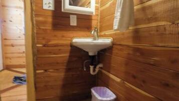 Une petite salle de bain aux murs lambrissés, avec un lavabo blanc, un miroir et une poubelle.