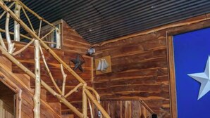 Ein rustikaler Holzinnenraum mit einer Holztreppe, einer blauen Wand mit einem weißen Stern und einem schwarzen Schrank mit einem Bücherstapel.
