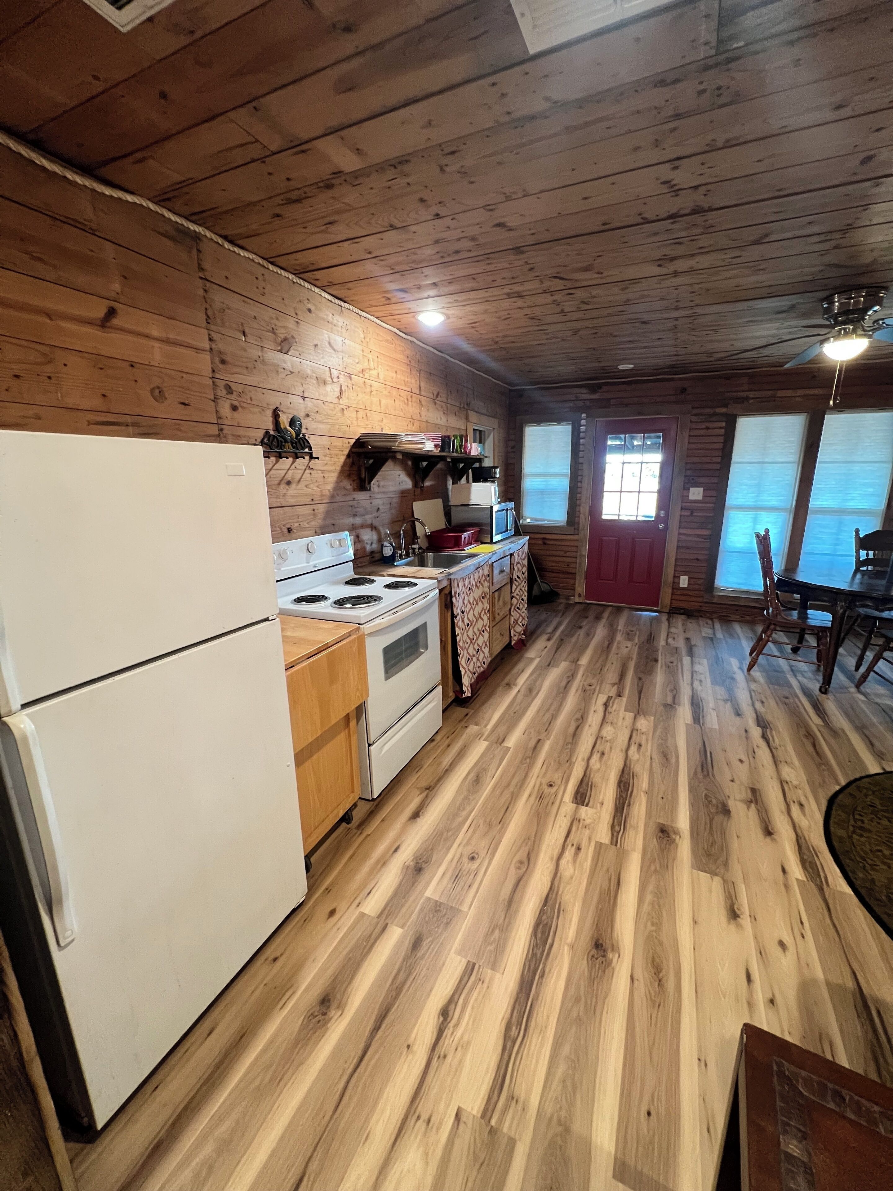 A wooden cabin kitchen with a refrigerator, stove, microwave, and wooden cabinets.