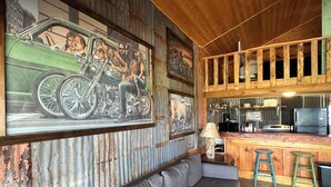 A rustic interior with a wooden ceiling, a grey sofa, a bar area, and a motorcycle mural on the wall. - Center Stage @ Yellow Rose Canyon (Rusk County)