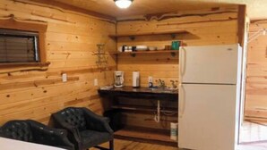 A wooden cabin interior with a bed, a kitchenette, and a refrigerator. - Barn 1 @ Yellow Rose Canyon (Rusk County)