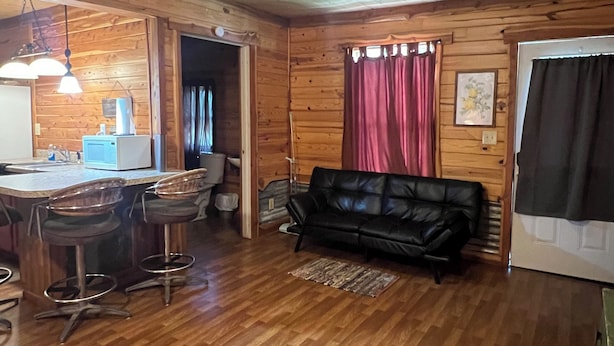 A wooden interior with a kitchen area, a black leather sofa, and a dining table with bar stools. - The Hideout @ Yellow Rose Canyon (Rusk County)