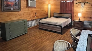 A wooden-paneled room with a bed, dresser, wicker chairs, and a table. - The Hideout @ Yellow Rose Canyon (Rusk County)