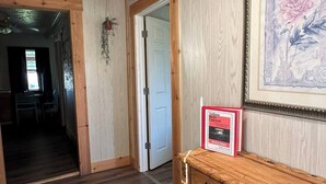 A spacious room with wooden flooring, a wooden bench, a framed painting, and a welcome sign.