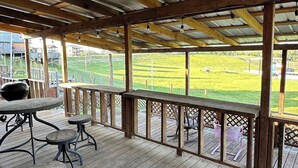 An outdoor wooden deck with metal railings, a barbecue grill, and tables.