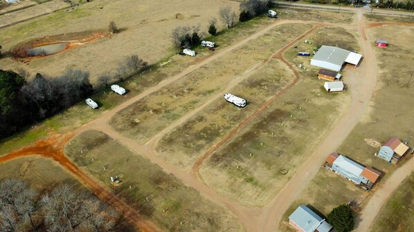 An aerial view of a rural property with multiple rectangular plots, some with buildings and others with open fields. There are several white trailers and a few small structures.