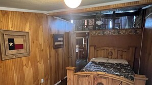 A wooden bedroom with a bed, a ceiling light, and a Texas flag on the wall.