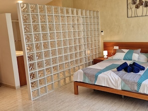 A bedroom with a bed, a nightstand, a wall-mounted lamp, and a decorative panel.