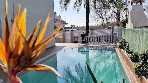 Une piscine offrant une vue dégagée sur les environs, notamment un bâtiment blanc, des palmiers et une clôture.