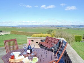 Mesa dispuesta al aire libre con botella de vino, copas, queso, uvas y pan.