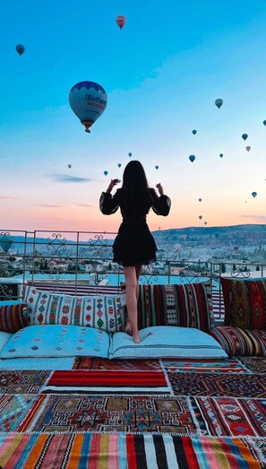 A person standing on a sofa overlooking a cityscape with hot air balloons in the sky. - Virtus Cappadocia Hotel (Nevsehir)