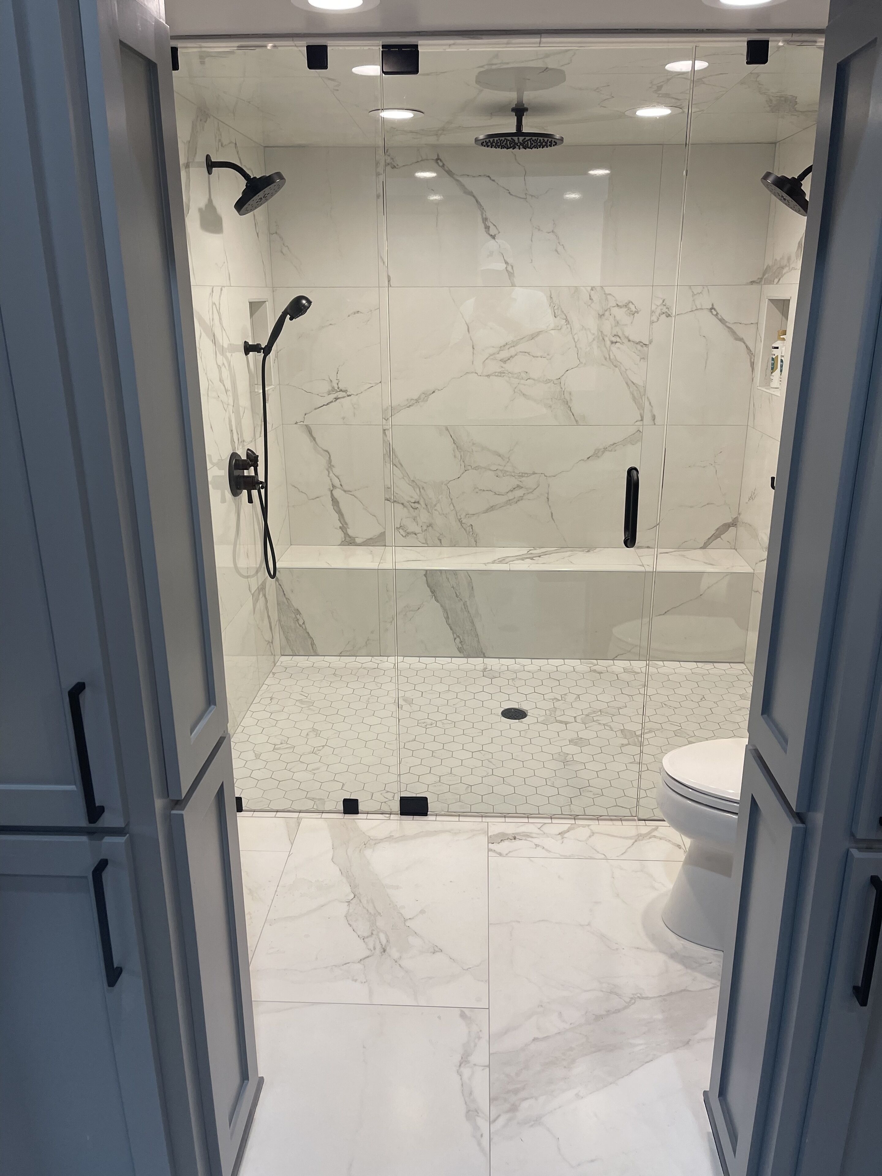 A modern bathroom with a glass-enclosed shower, marble tiles, a toilet, and a sink.