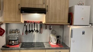 Una cocina compacta con armarios de madera, horno integrado, refrigerador y varios utensilios de cocina colgados en la pared.