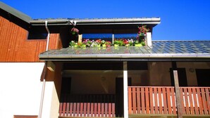 Un edificio con techo inclinado, un balcón con barandillas de madera y macetas con flores en el techo.
