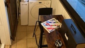 Un lavadero pequeño con lavadora, secadora, un reloj en la pared y una ventana con vistas a la calle y edificios.