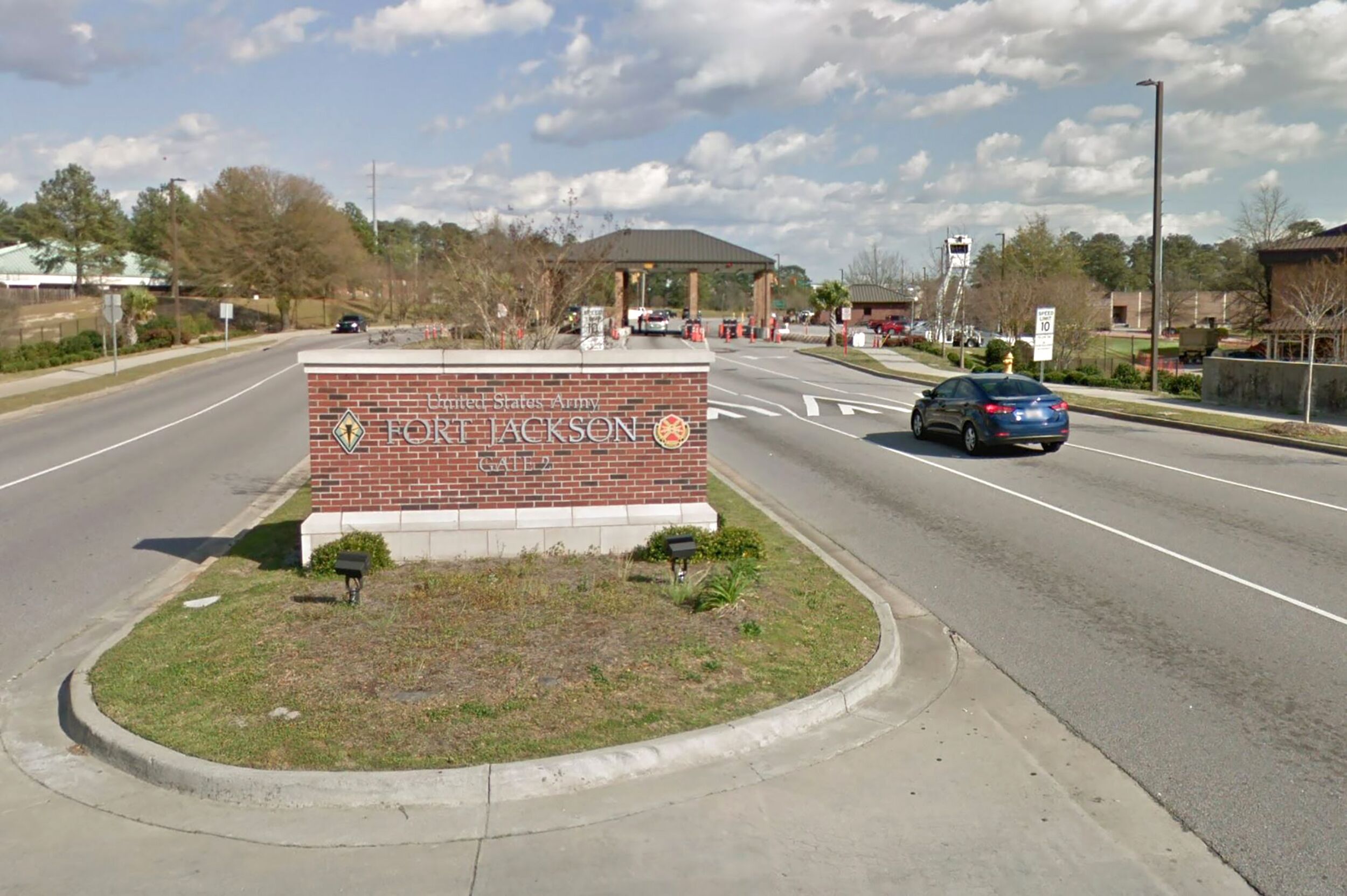 Un panneau de signalisation indiquant la direction de Fort Jackson, avec en arrière-plan un bâtiment en briques et une zone herbeuse au premier plan.