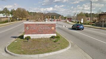 Un panneau de signalisation indiquant la direction de Fort Jackson, avec en arrière-plan un bâtiment en briques et une zone herbeuse au premier plan.