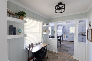 A kitchen with white cabinets, a dining area with a table and chairs, and a window with blinds. - Cute n' Comfy Capers (Columbia)