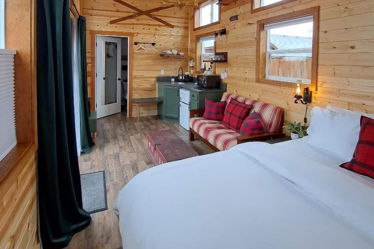 A wooden cabin interior with a bed, sofa, kitchenette, and a dining table.