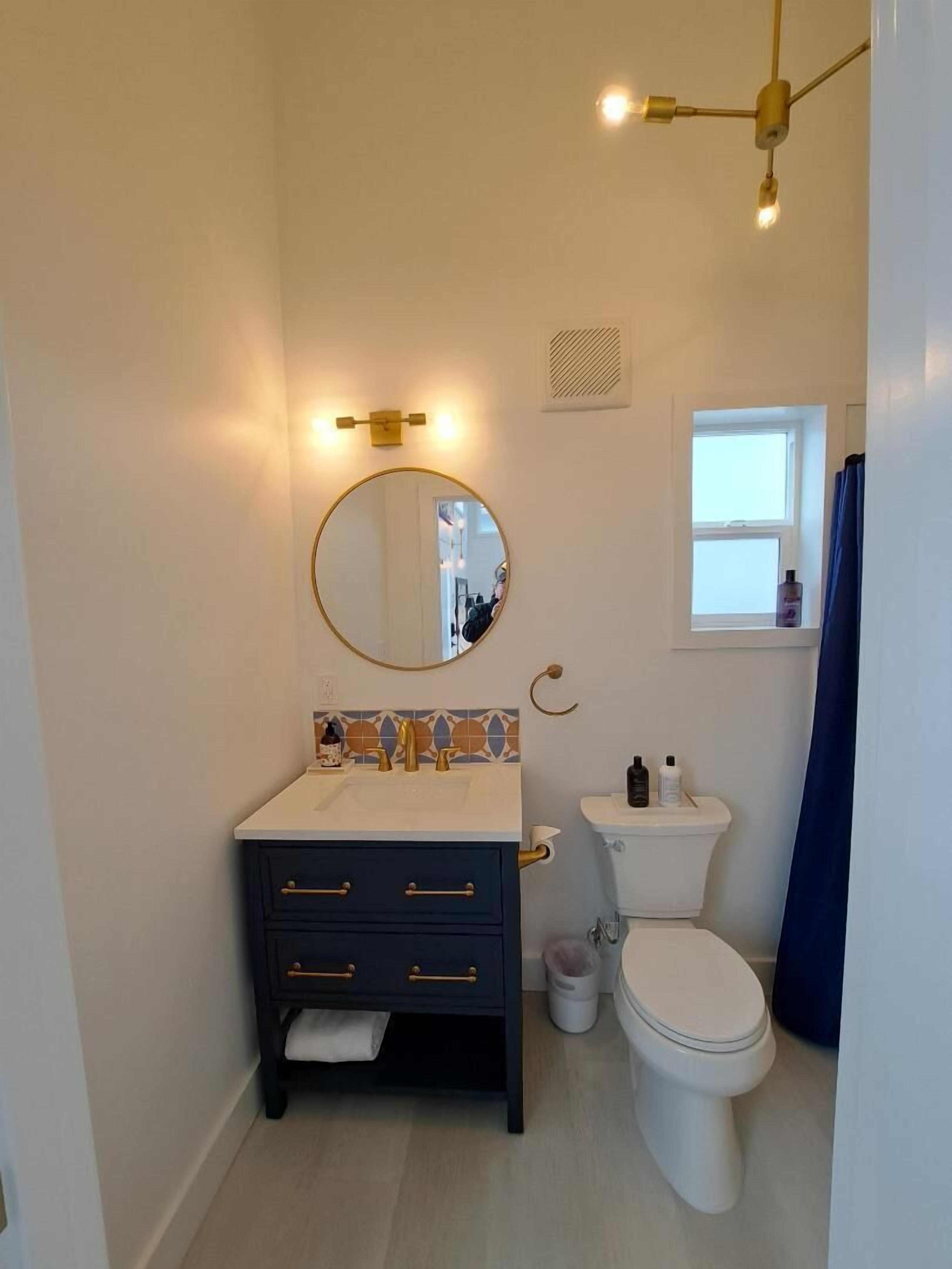 Een badkamer met een witte wastafel, donker aanrecht, ronde spiegel en wit toilet.