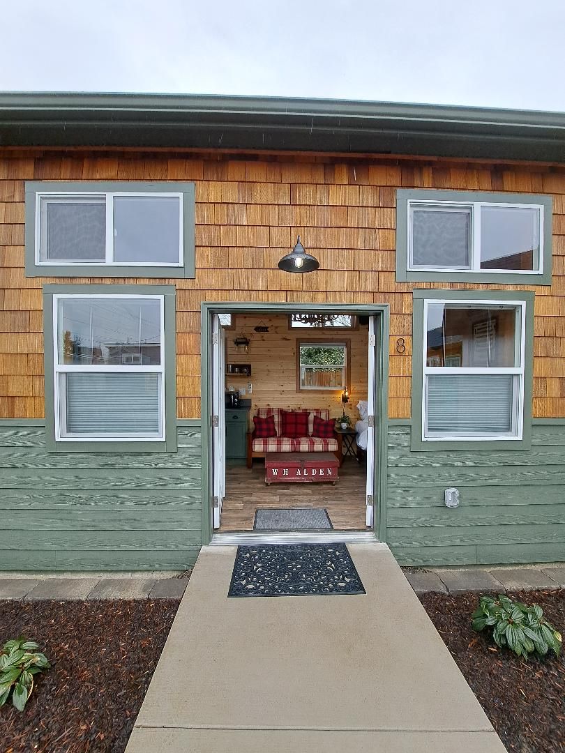 Un edificio de madera con fachada verde, una puerta principal y un interior visible con un sofá rojo y un letrero que dice 'W. Alden'.