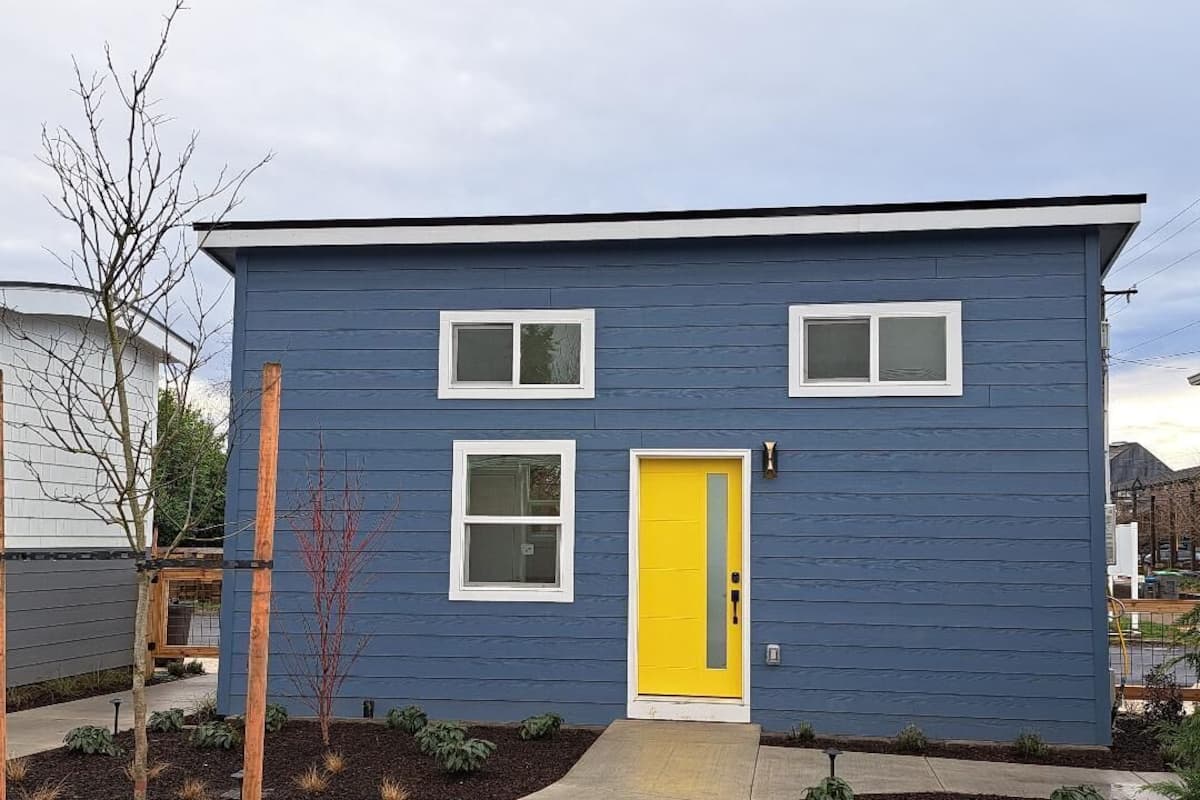 A two-story house with a yellow front door, white-framed windows, and a blue exterior.
