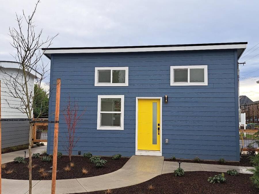 A two-story house with a yellow front door, white-framed windows, and a blue exterior.