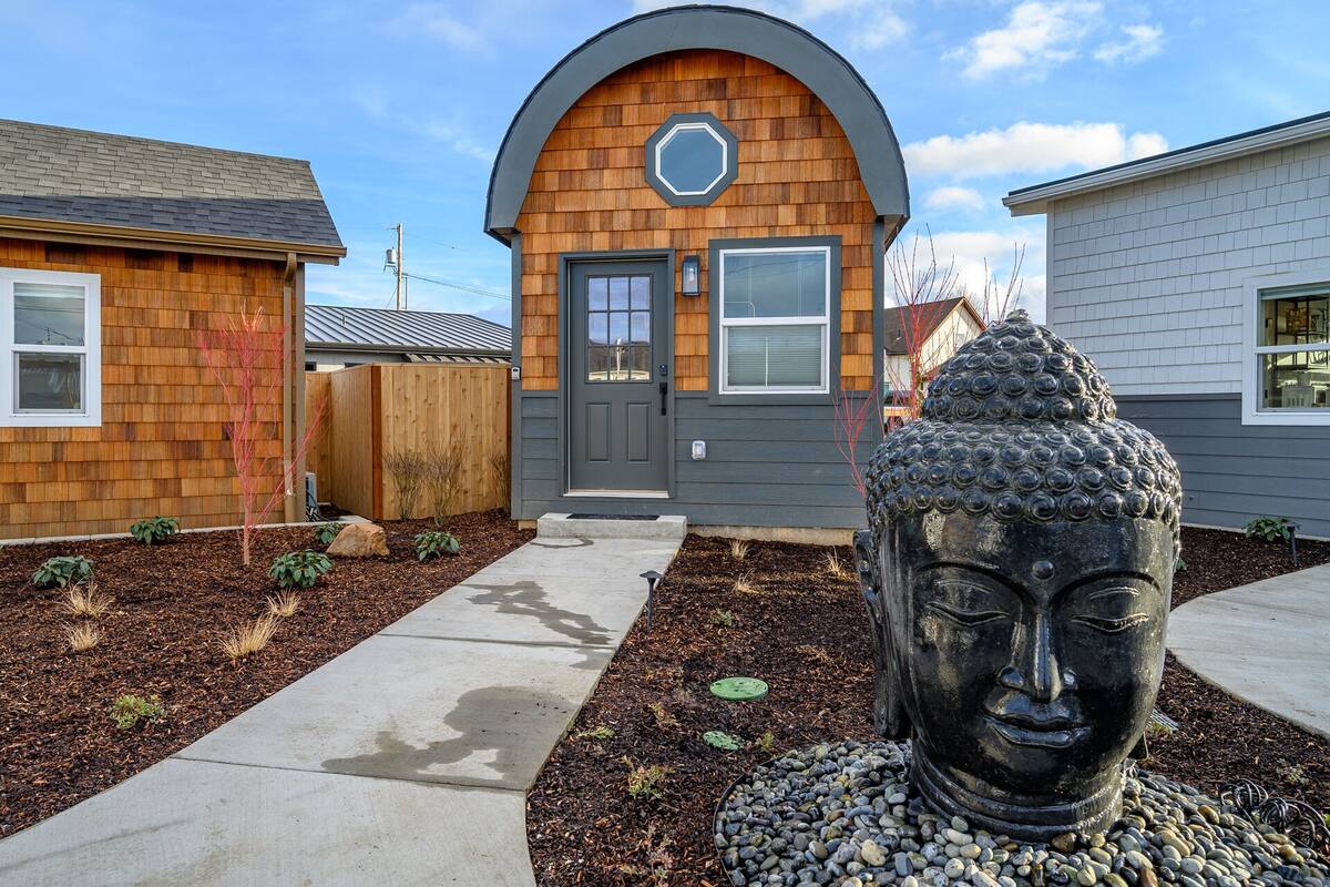 A modern house with a wooden facade, a grey door, and a large Buddha statue in the front yard.