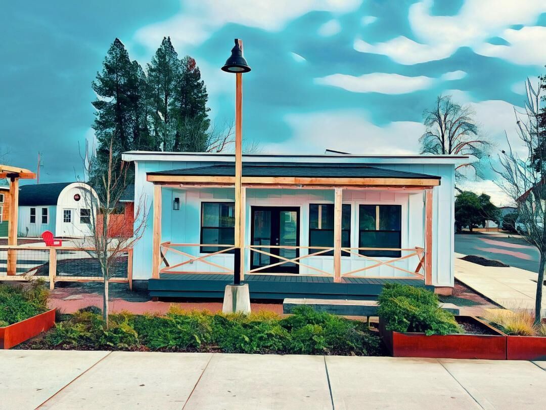 A small, single-story building with a flat roof, large windows, and a simple, open porch area.