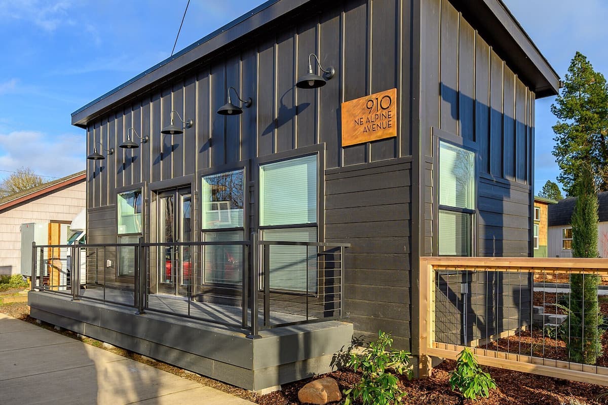 A modern building with a sign reading '910 NE ALPINE AVENUE,' large windows, and a metal exterior.