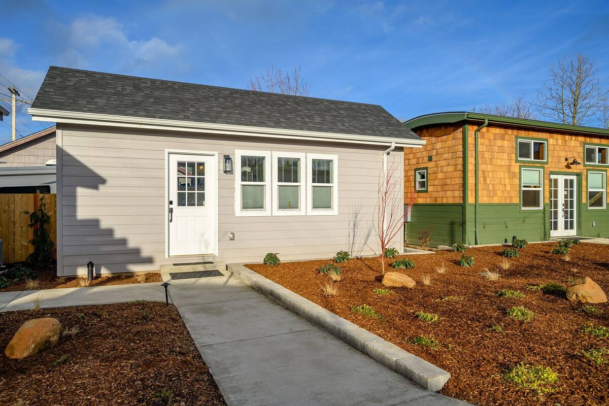 A two-story house with a front porch, a small garden with mulch and plants, and a clear blue sky.