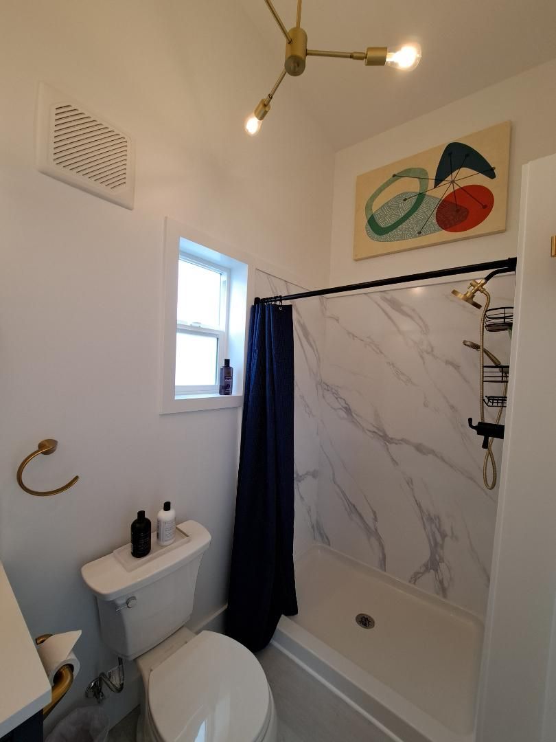 A bathroom with a toilet, sink, shower, and a window.