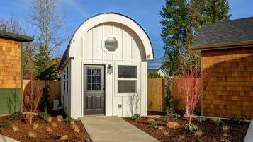 A small, white, semi-circular structure with a door and windows, surrounded by a wooden fence and a landscaped garden.