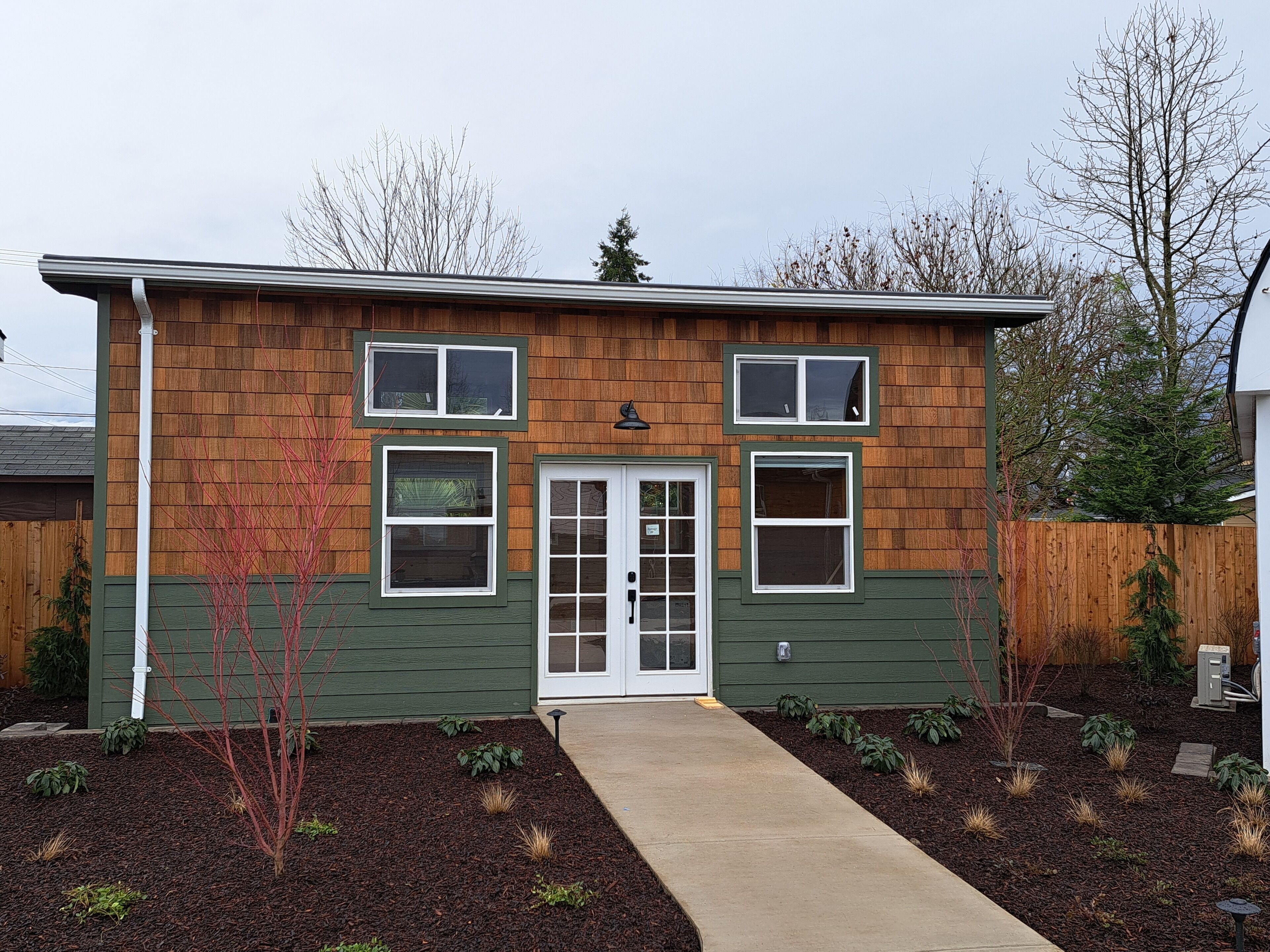 A two-story house with a front door, two windows on the upper floor, and a small front yard with mulch and plants.