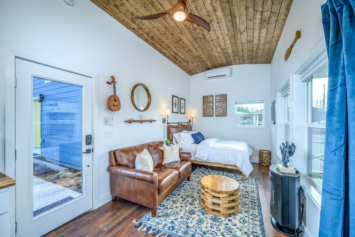 A bedroom with a wooden ceiling, a bed, a brown leather sofa, a wooden coffee table, and a fireplace.