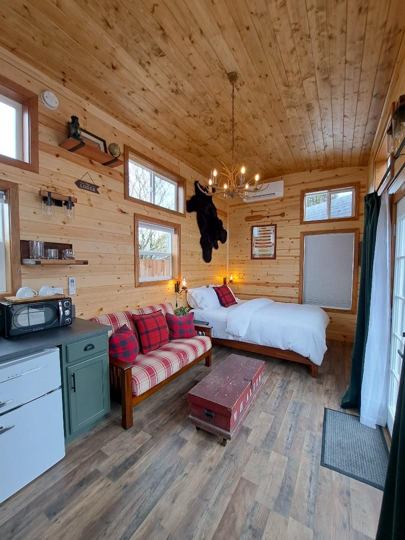 A cozy cabin interior with a bed, sofa, kitchenette, and a hanging coat rack.