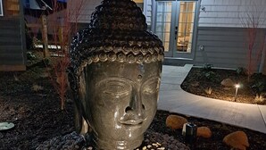 Una gran estatua de Buda en un jardín con guijarros y un sendero que conduce a un edificio.