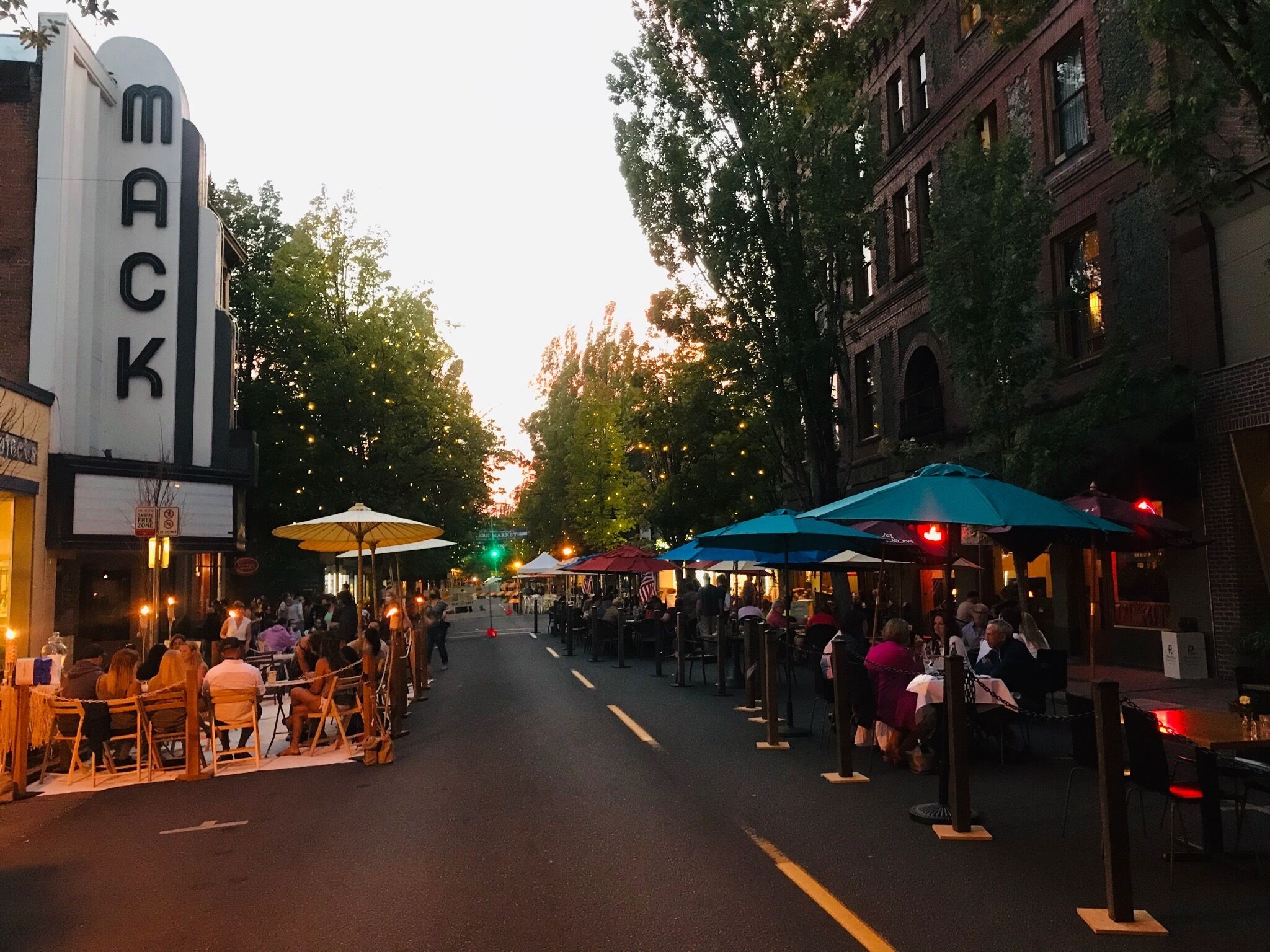 A street lined with outdoor seating areas, a marquee sign, and brick buildings.