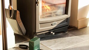 En vedeldad kamin med synliga lågor, ett par saxar och en grön låda med texten ”Tändstickor” på, placerat på ett klinkergolv.